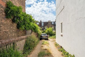 Uma viela estreita com um carro estacionado, paredes de tijolo e um edifício branco.