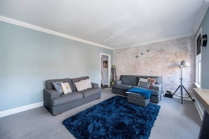 A living room with two grey sofas, a blue rug, and a brick wall.