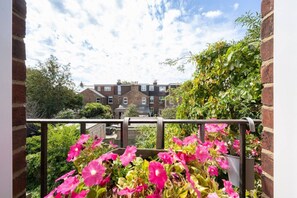 A balcony with a view of a residential area, featuring a brick wall and a metal railing.