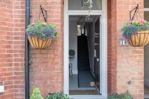 A brick building entrance with two hanging flower baskets and a door marked with the number 18.
