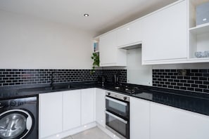 A compact kitchen with white cabinets, a black countertop, a washing machine, and a built-in oven.