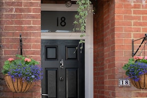 A black door with the number 18 above it, flanked by hanging flower baskets.