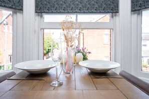 A dining table set with two plates, a wine glass, and a vase with dried flowers.