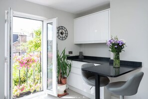 A modern kitchen with a black countertop, two grey chairs, a potted plant, and a wall clock.