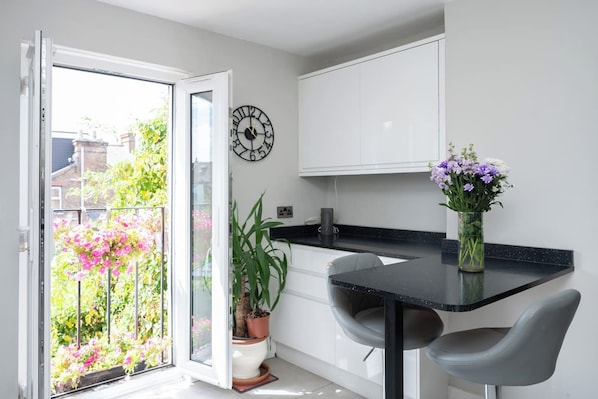 A modern kitchen with a black countertop, two grey chairs, a potted plant, and a wall clock.