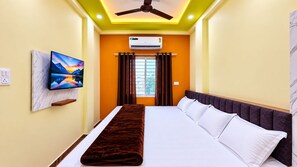 A hotel room with a bed, a television mounted on the wall, an air conditioning unit, and a window with curtains. - Shree Bada Ganesh Yatri Grah (Ujjain)