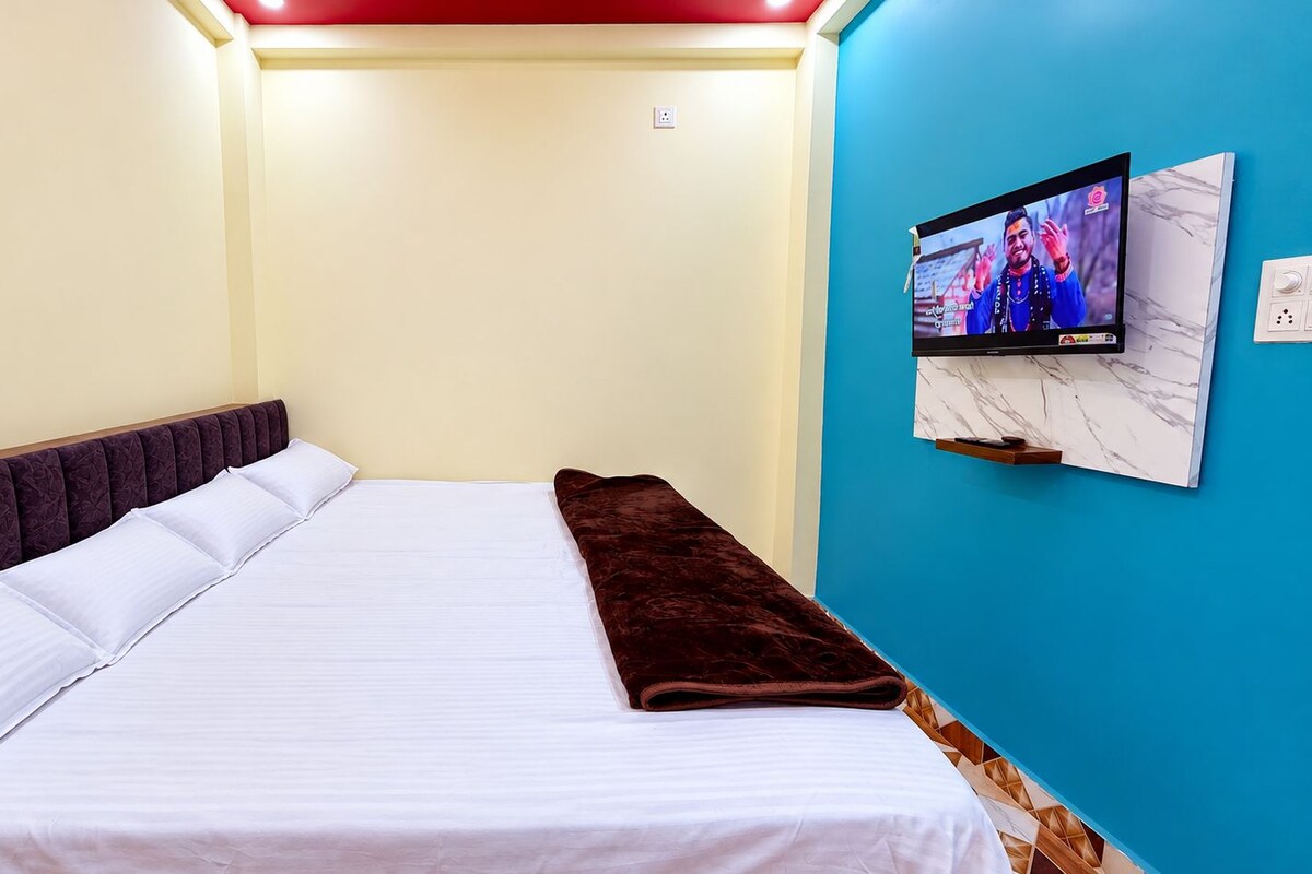 A hotel room with a bed, a television on the wall, and a blue accent wall.
