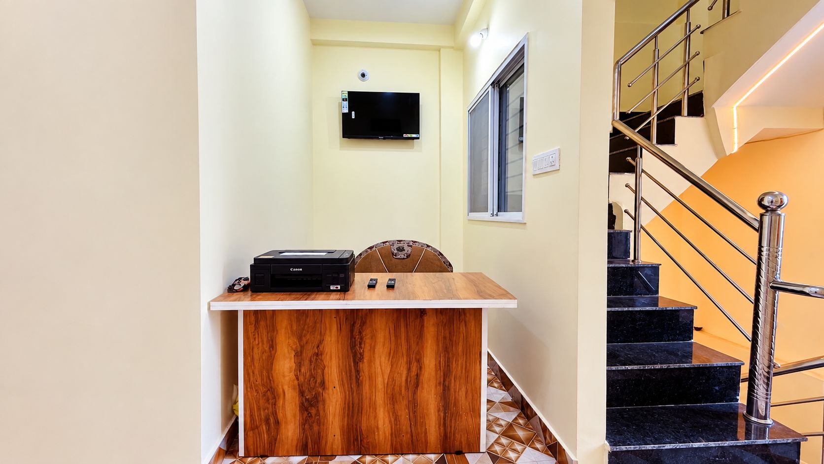 Habitación de hotel con un escritorio de madera, un televisor de pantalla plana montado en la pared y una escalera con barandillas de metal.