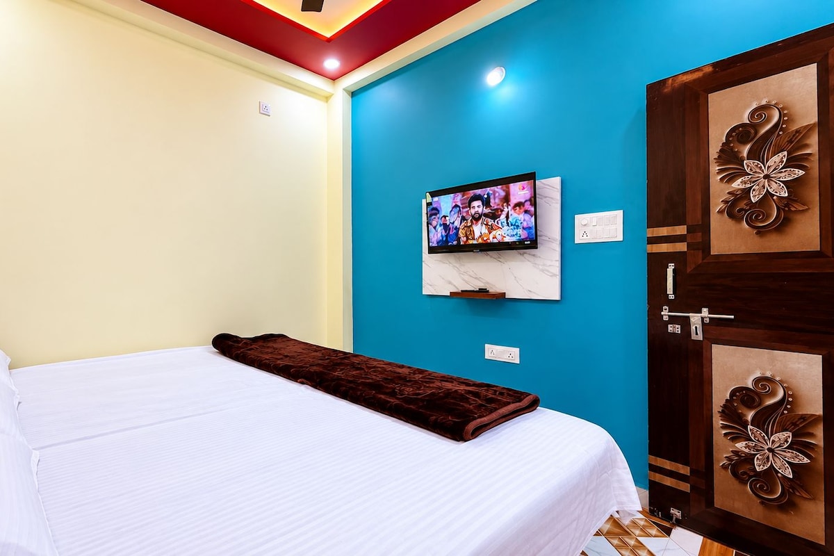 Una habitación de hotel con cama, televisor montado en la pared y puerta con paneles decorativos.