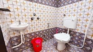Un baño con un lavamanos blanco, un inodoro y un balde rojo.