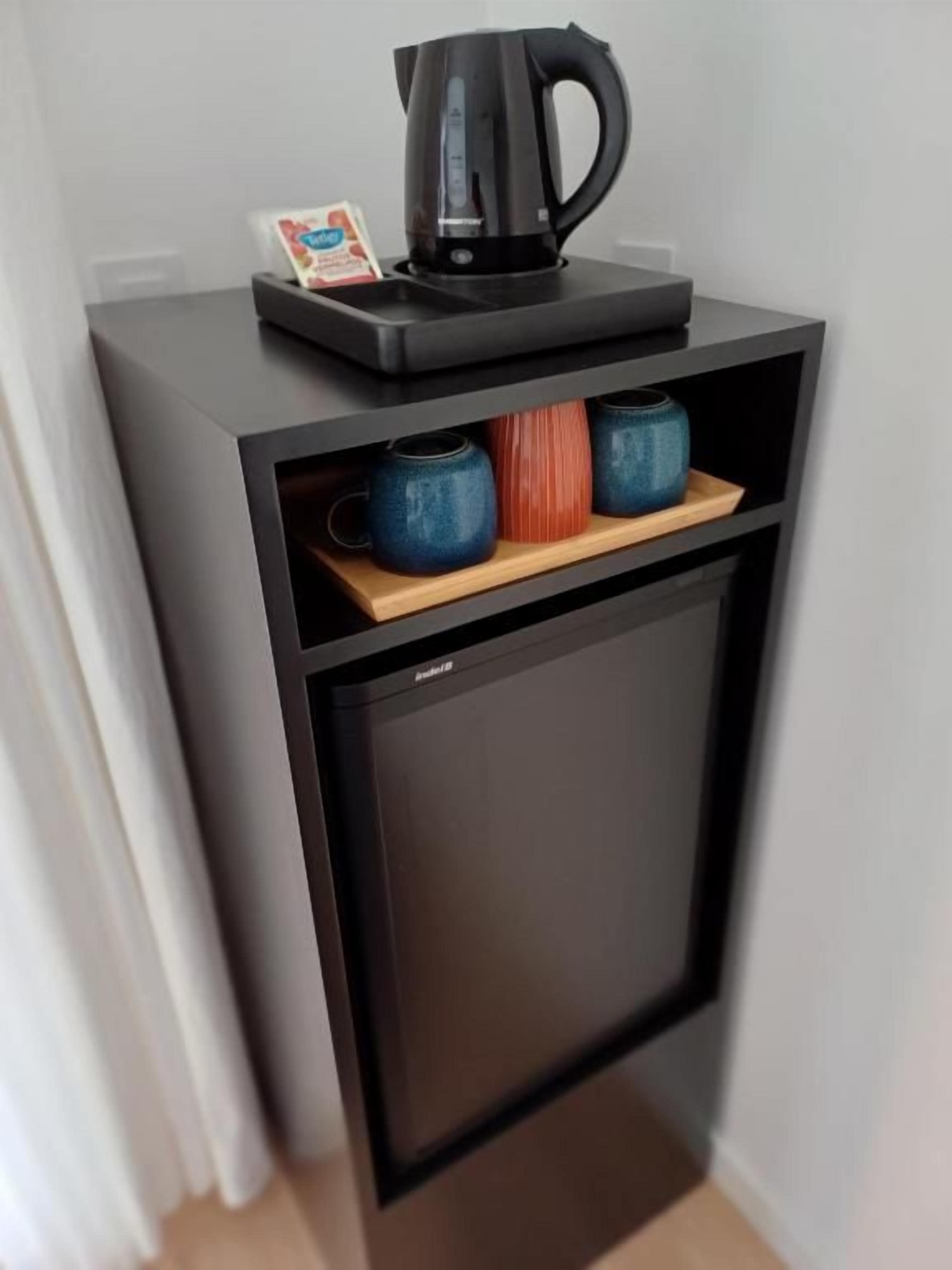 A compact black refrigerator with a coffee maker and mugs on top.