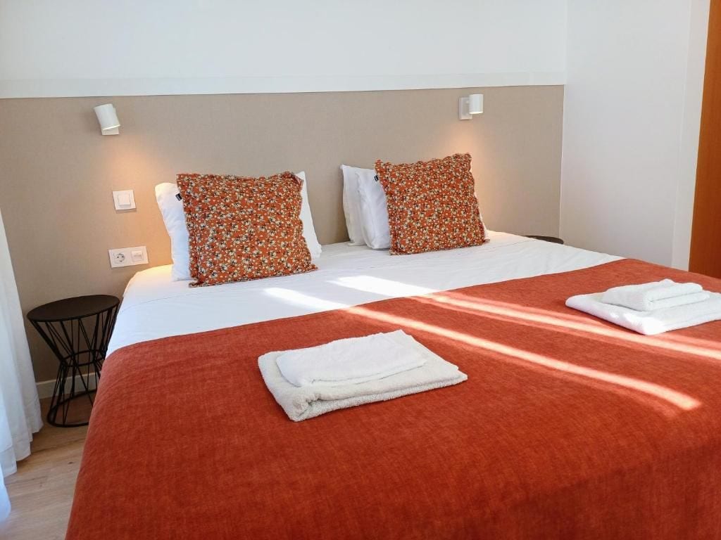 A hotel room with a bed, pillows, a small round table, and a wall-mounted light.