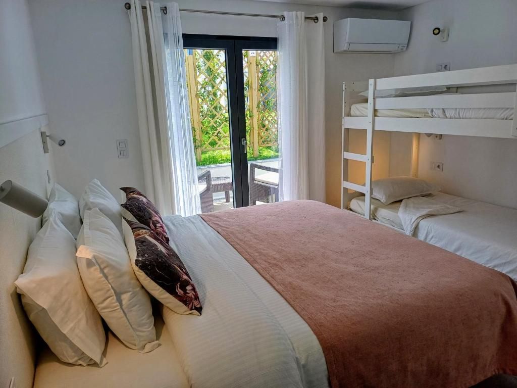 A bedroom with a bed, a bunk bed, a window with curtains, and an air conditioning unit.