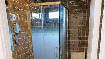 A bathroom with a glass-enclosed shower, a toilet, and a sink.