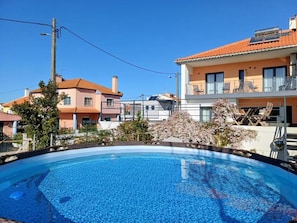 A swimming pool with a clear blue surface, surrounded by residential buildings with balconies and a clear sky.