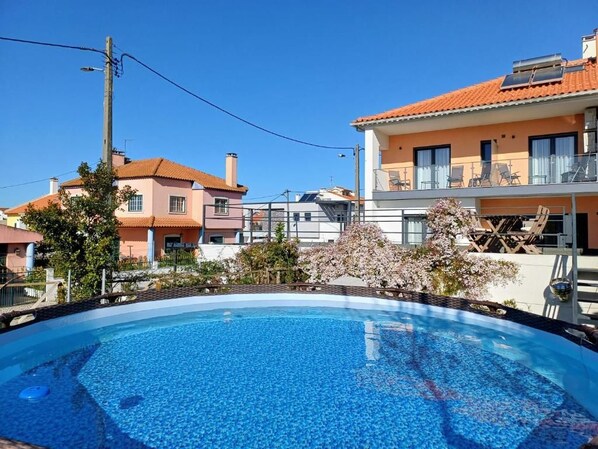 A swimming pool with a clear blue surface, surrounded by residential buildings with balconies and a clear sky.