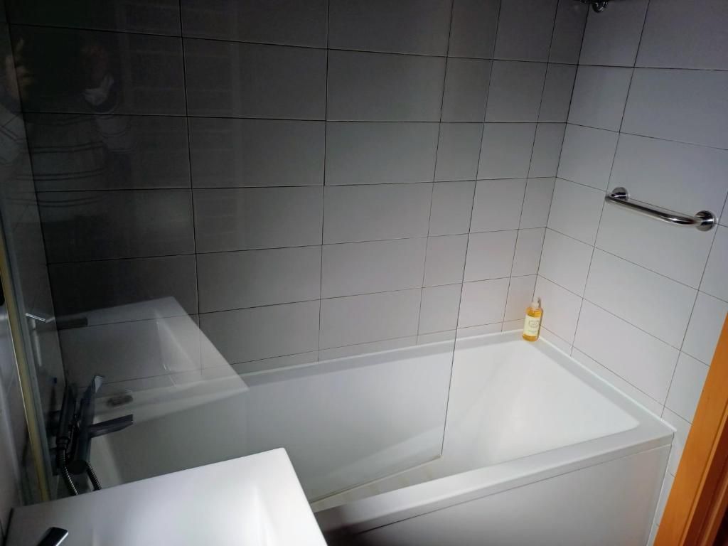 A bathroom with a bathtub, a glass shower enclosure, and a handrail on the wall.