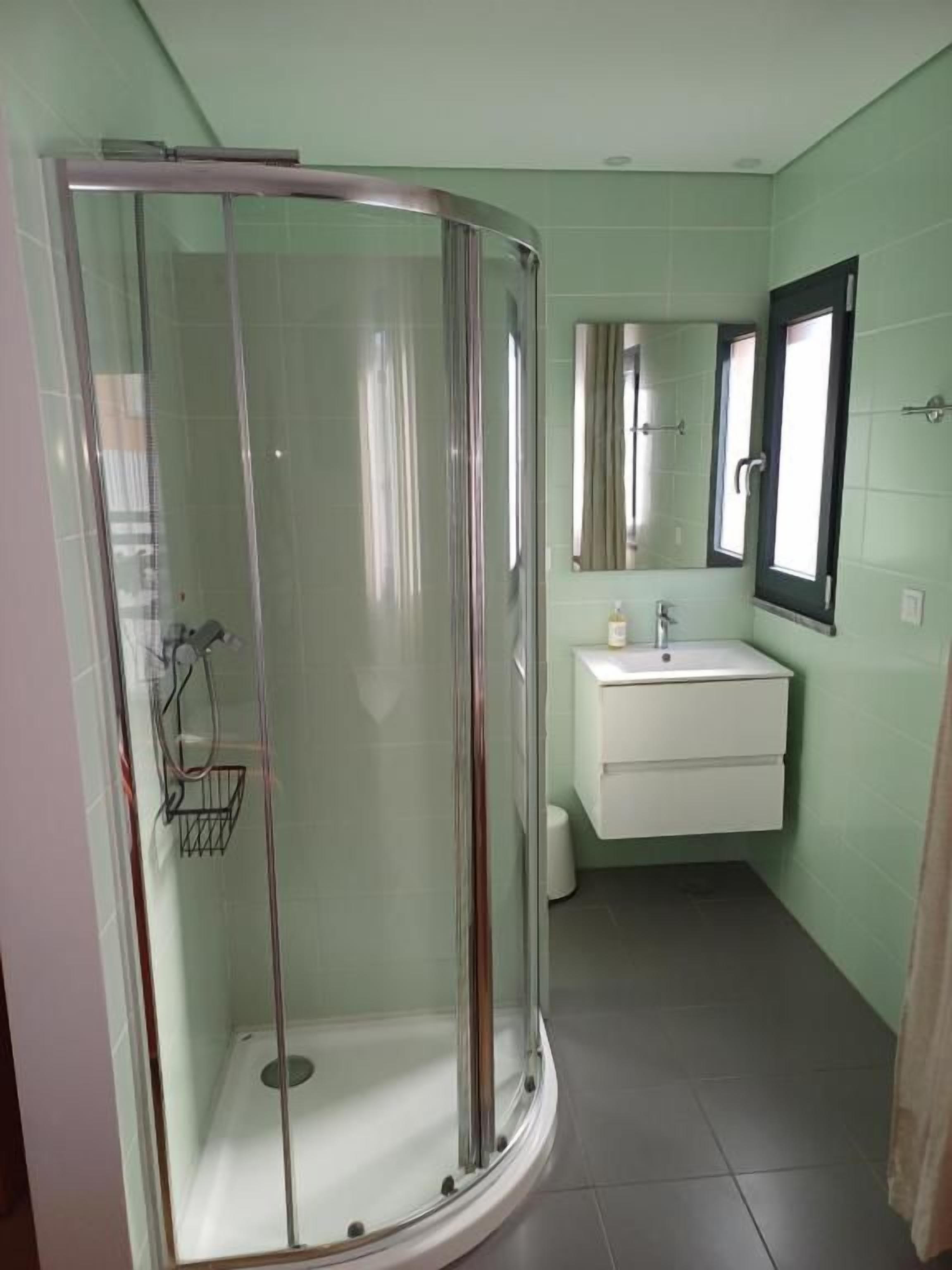 A bathroom with a glass-enclosed shower, a white sink, and a mirror above the sink.