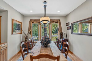 A dining area with a long wooden table, chairs, a chandelier, and large windows with curtains. - Keystone Ranch Escape | Hot Tub + Grill + Deck (Dillon)