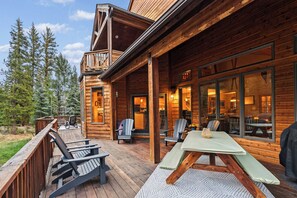 Eine Holzhütte mit einer Terrasse, Sitzgelegenheiten im Freien und großen Fenstern.