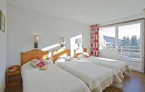 Habitación de hotel con dos camas, un cabecero de madera, una ventana con vistas al exterior y una mesita de noche de madera.