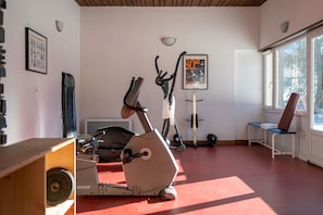 A gym with exercise equipment, a poster on the wall, and a window with a view of trees.