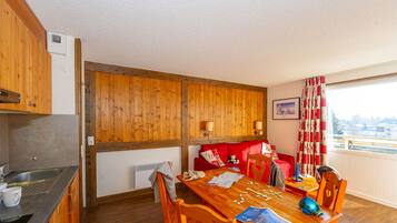 A cozy room with a wooden dining table, chairs, a red sofa, and a window with curtains.