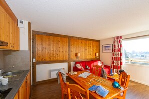 A cozy room with a wooden dining table, chairs, a red sofa, and a window with curtains.