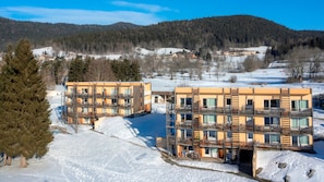 A modern multi-story building with balconies, surrounded by snow-covered landscape and trees.