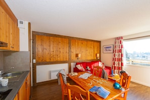 A cozy room with a wooden dining table, chairs, a red sofa, and a window with curtains.