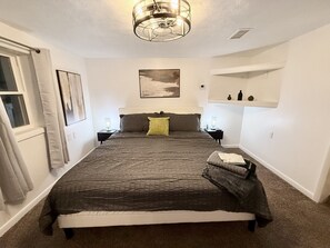 A bedroom with a large bed, a ceiling light fixture, a wall-mounted shelf with decorative items, and a window with curtains. - Delightful Quiet 3 BR 2 bath home in Carnegie (Carnegie)