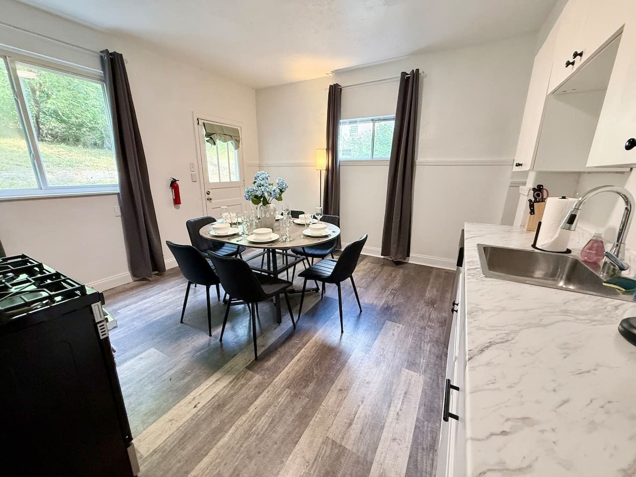 A dining area with a table set for four, a kitchen with a sink and cabinets, and a fire extinguisher on the wall.