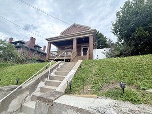 Ein zweistöckiges Gebäude mit einer Veranda und einer Betontreppe, die zum Eingang führt.