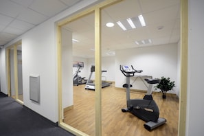 A gym with exercise equipment, including treadmills and an elliptical, with a wooden floor and white walls. - Au cœur de Vaujany | Piscine | Télécabine à 600 m (Vaujany)