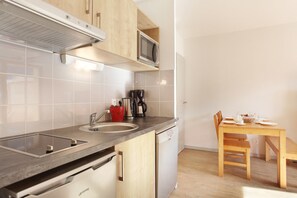 A compact kitchen with a microwave, coffee maker, and a dining area with a table and chairs. - Au cœur de Vaujany | Piscine | Télécabine à 600 m (Vaujany)