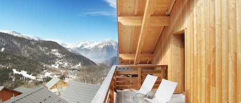 Un balcón de madera con dos sillas blancas, con vistas a un paisaje montañoso nevado.