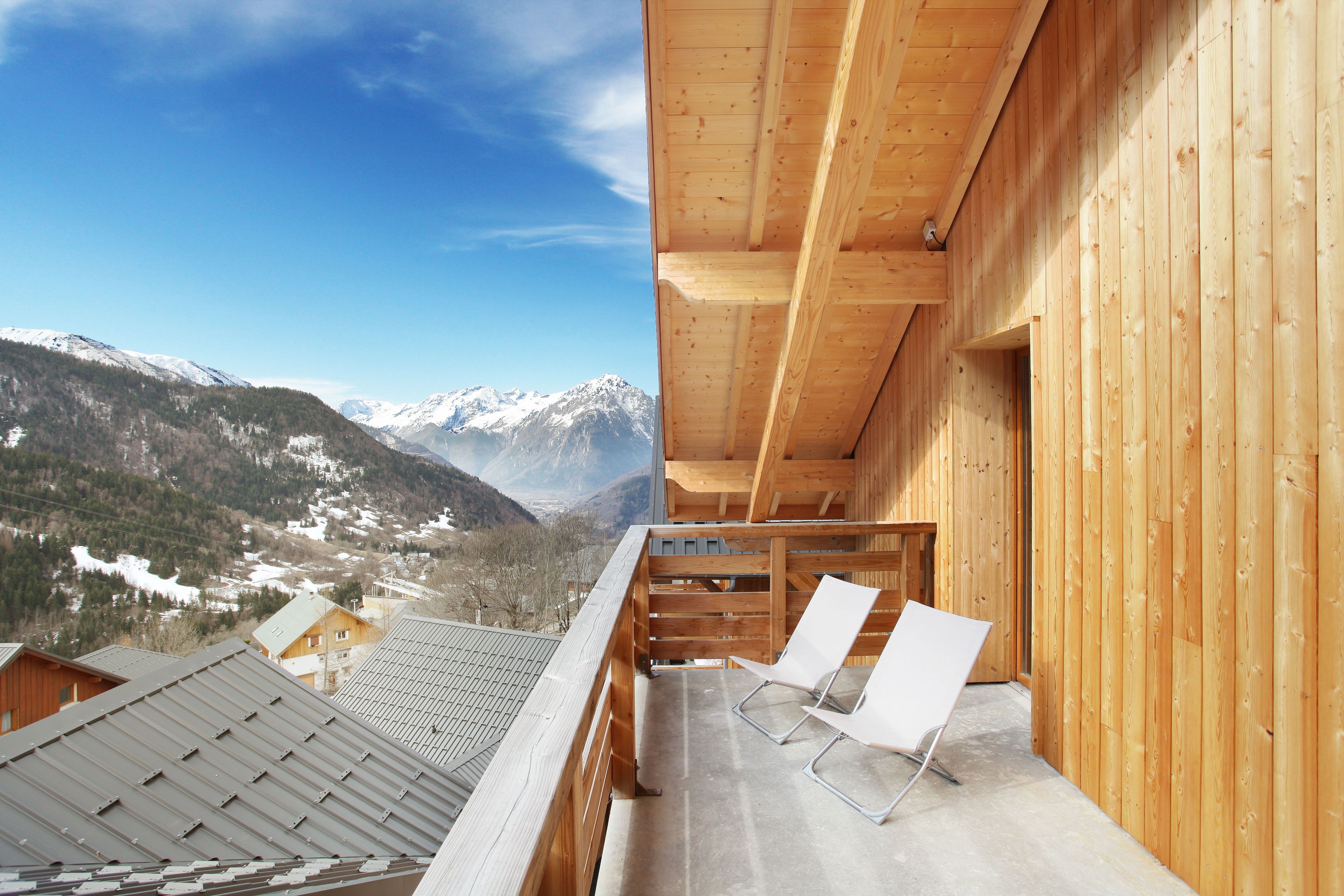 Un balcón de madera con dos sillas blancas, con vistas a un paisaje montañoso nevado.