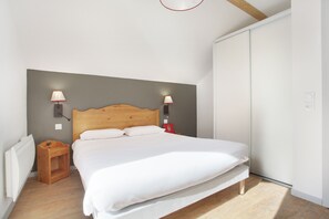 A bedroom with a wooden headboard, a bed with white bedding, two bedside lamps, a nightstand, and a wardrobe. - Vue sur les montagnes | Piscine | Télécabine 600 m (Vaujany)