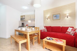 Ein kompakter Wohnbereich mit Essplatz, Küchenzeile und einem roten Sofa mit gemusterten Kissen.