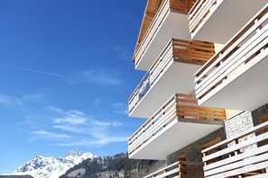 Ein mehrstöckiges Gebäude mit Balkonen, blauem Himmel und Bergen im Hintergrund.
