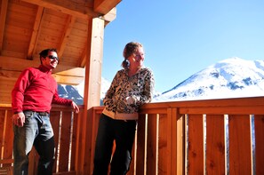 Two individuals standing on a wooden balcony with a mountain view in the background. - Piscine chauffée | Sauna gratuit | Vue montagne (Saint-Jean-d'Arves)