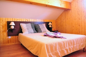 A bedroom with a wooden headboard, two bedside lamps, a bed with a striped pillow, and a blanket. - Piscine chauffée | Sauna gratuit | Vue montagne (Saint-Jean-d'Arves)