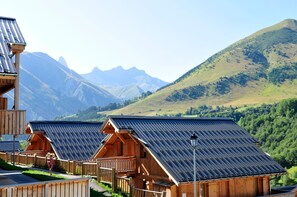 A row of wooden cabins with sloped roofs, set against a backdrop of mountains and a clear sky. - Piscine chauffée | Sauna gratuit | Vue montagne (Saint-Jean-d'Arves)