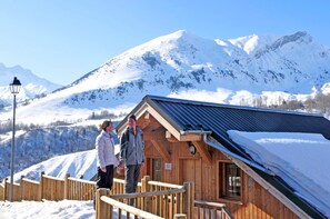 Eine Holzhütte mit geneigtem Dach, einem Holzzaun und einem schneebedeckten Berg im Hintergrund.