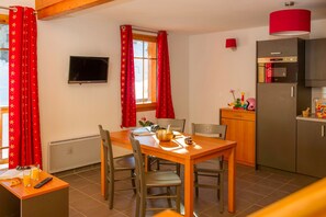 Una cuina compacta amb taula de dinar, cadires, televisió i nevera.