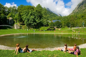 A lake with people relaxing on the grass, a picnic area, and a mountain in the background. - Proche des pistes | Piscine & Sauna sur place (Saint-Colomban-des-Villards)