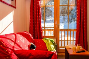 Ein gemütliches Zimmer mit einem roten Sofa, einer Holztür, die nach draußen führt, und einem kleinen Tisch mit Gläsern und einer Fernbedienung.