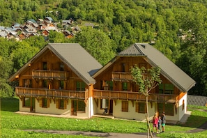 Eine Holzchalet mit Balkon, eingebettet in ein üppiges, grünes Tal, mit weiteren Gebäuden im Hintergrund.