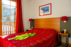 Ein Hotelzimmer mit einem Bett, einem Fenster mit Vorhängen, einem gerahmten Bild an der Wand und einem Nachttisch mit einer Lampe.