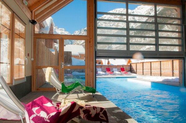 A pool area with lounge chairs and a view of snowy mountains through large windows.